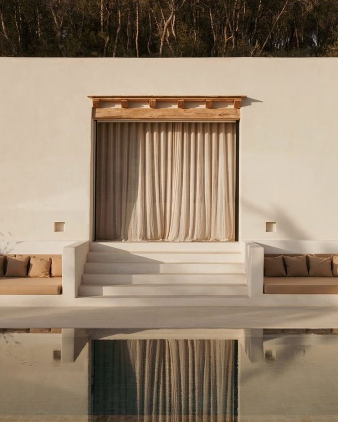 Fachada blanca de una propiedad mediterránea reflejada en la piscina.